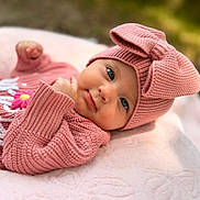 Lainey is registered to the contest to win money with this photo: baby, pink, knitwear, hat, bow, blanket, infant, cute, portrait, face, hand, outdoor, soft, cozy, child, apparel, warm, lying_down, expression, closeup