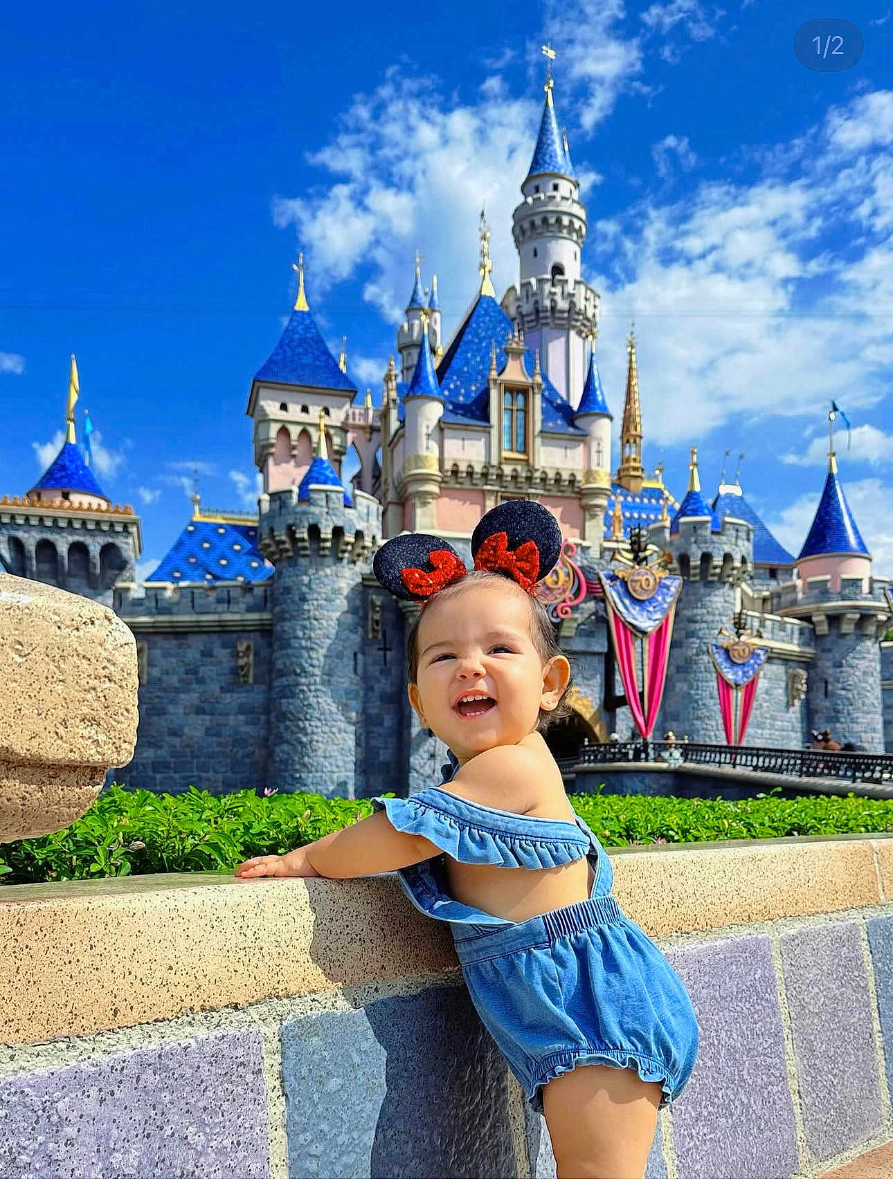 Isabella joined the competition — help win amazing prizes! toddler, child, blue_romper, minnie_mouse_ears, castle, disney, stone_wall, greenery, blue_sky, clouds, happy, smile, outdoor, sunny, theme_park, architecture, tourist, holiday, playful, portrait