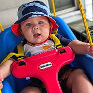 Jasper is registered to the contest to win money with this photo: baby, child, swing, bucket_hat, blue_eyes, red_swing, yellow_straps, outdoor, porch, summer_clothing, sun_shirt, happy, curious, playtime, infant, seat, plastic_toy, closeup, smiling, person