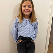 Shayness participe au concours pour gagner de l'argent avec cette photo : child, girl, smiling, standing, blue_blouse, striped_clothing, ruffled_collar, dark_pants, hands_in_pockets, indoor, plain_wall, casual_pose, long_hair, portrait, person, happy, fashion, young, cute, confident