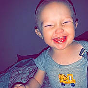 Greyson is registered to the contest to win money with this photo: arm, bed, blanket, buzz_cut, child, close_up, clothing, embroidered_truck, eyes_squinting, face, hand, happy, indoor, laughing, onesie, portrait, skin, smiling, teeth, toddler