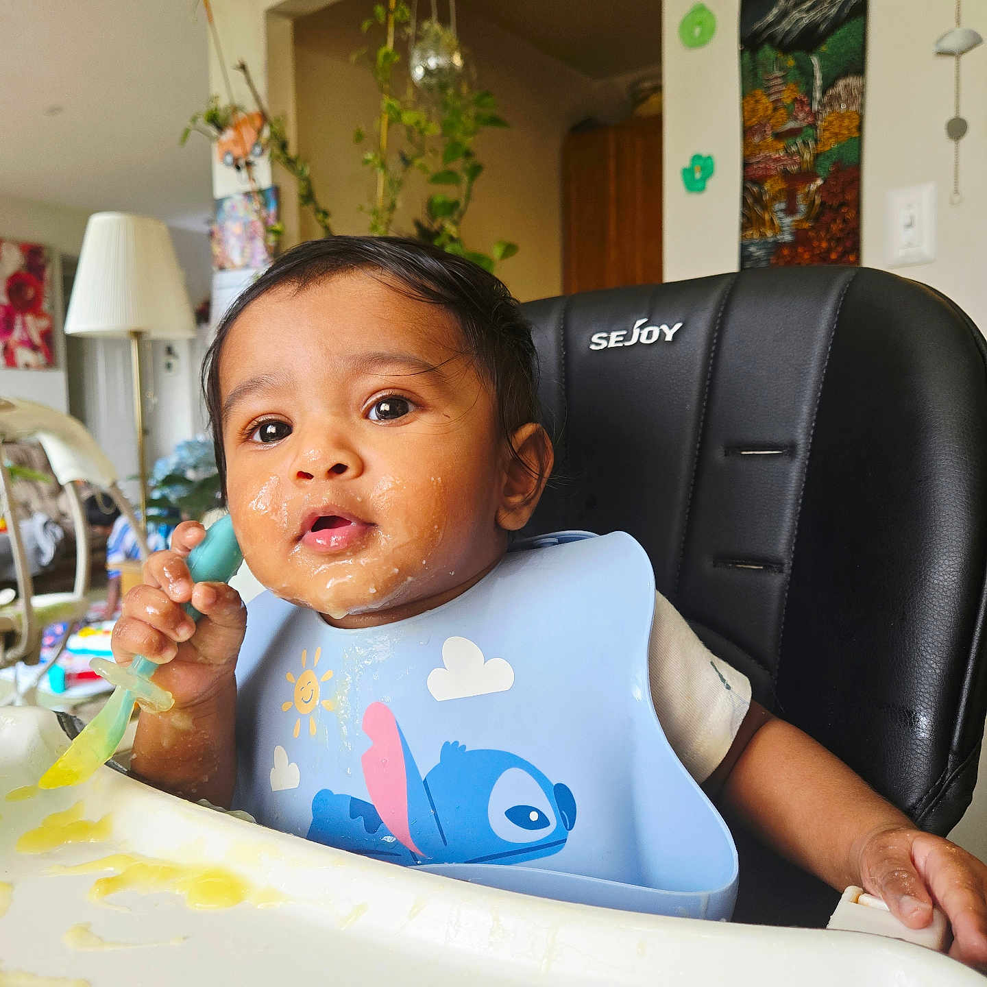 Krishnendu joined the competition — help win amazing prizes! baby, child, high_chair, bib, spoon, food, messy, face, indoor, home, plant, furniture, cute, infant, feeding, expression, person, seat, wall_decor, kitchen