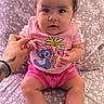 baby, child, girl, pigtails, pink_clothing, cartoon_print, tattoo, hand_holding, couch, floral_pattern, indoors, cute, portrait, sitting, barefoot, bracelet, expression, person, infant, home
