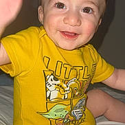 Noah is registered to the contest to win money with this photo: baby, child, smiling, yellow_shirt, star_wars, toddler, happy, face, eyes, hand, sitting, cute, indoors, clothing, infant, person, portrait, skin, short_hair, bed