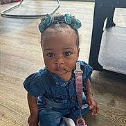 Keyoni is registered to the contest to win money with this photo: child, toddler, baby, denim, pacifier, blue_bows, curly_hair, indoor, wooden_floor, flooring, table, baby_rocker, clothing, cute, sitting, face, expression, hands, footwear, infant