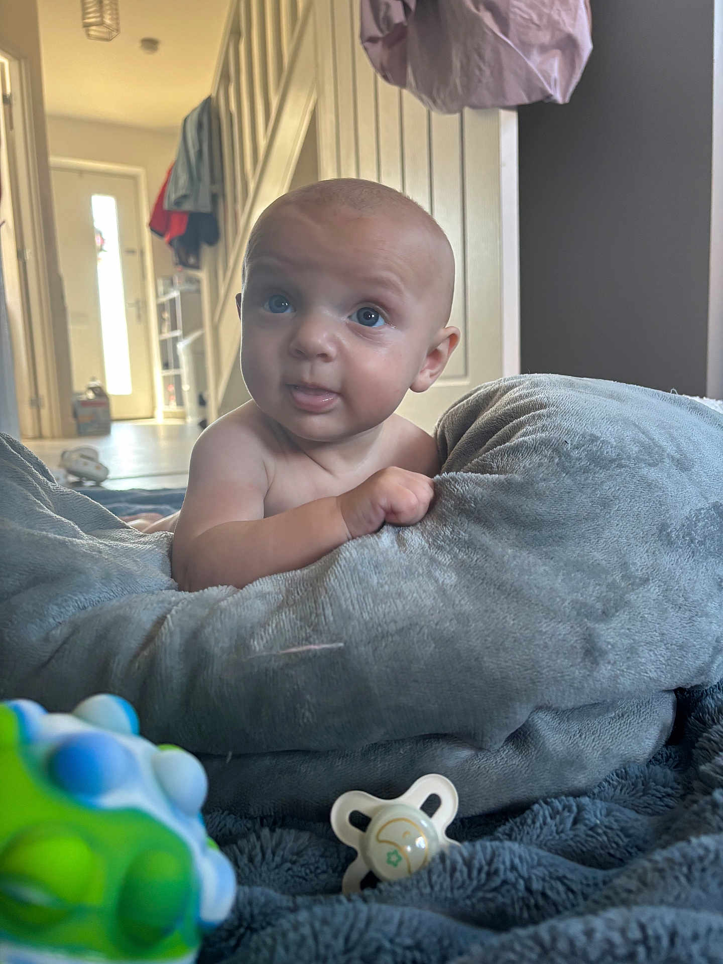 Oakley joined the competition — help win amazing prizes! baby, infant, blue_eyes, blanket, pacifier, toy, indoor, curious, face, skin, hand, soft_texture, floor, home, light, door, stairs, clothing, expression, child