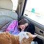 child, sleeping, cat, orange_cat, car_interior, window, tie_dye, hoodie, seat, blanket, resting, pet, whiskers, fur, curious, daylight, seatbelt, travel, relaxation, cozy