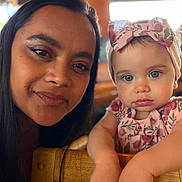 Zaliyah is registered to the contest to win money with this photo: woman, baby, child, face, portrait, headband, blue_eyes, floral_pattern, close_up, indoor, wooden_chair, person, cute, family, mother_and_child, skin, expression, looking_at_camera, casual, love