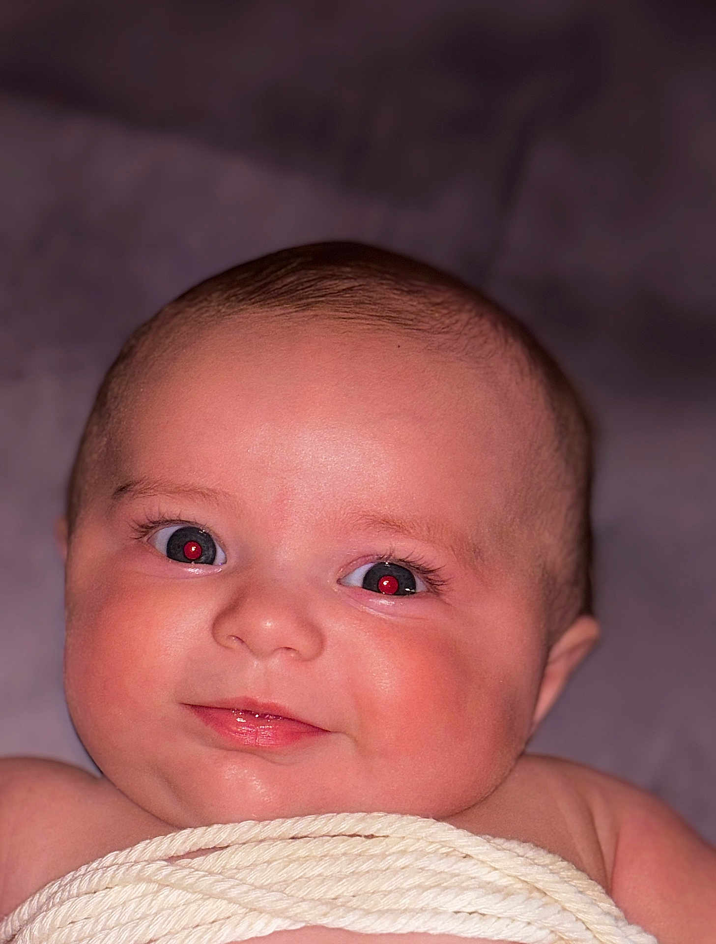 Paislee joined the competition — help win amazing prizes! baby, infant, face, eyes, red_eye, smile, chubby_cheeks, closeup, portrait, skin, eyelashes, forehead, mouth, lips, head, blanket, swaddle, lying_down, soft_lighting, indoor