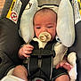 baby, newborn, infant, pacifier, car_seat, safety_harness, buckle, head_support, warning_label, strap, hand, leg, clothing, plush, indoors, portrait, seat, sleepy, baby_accessory, closeup
