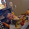 baby, smiling, activity_center, toy, indoor, child, happy, face, furniture, television, living_room, lion_toy, seat, playtime, person, home, wall, floor, clothing, infant