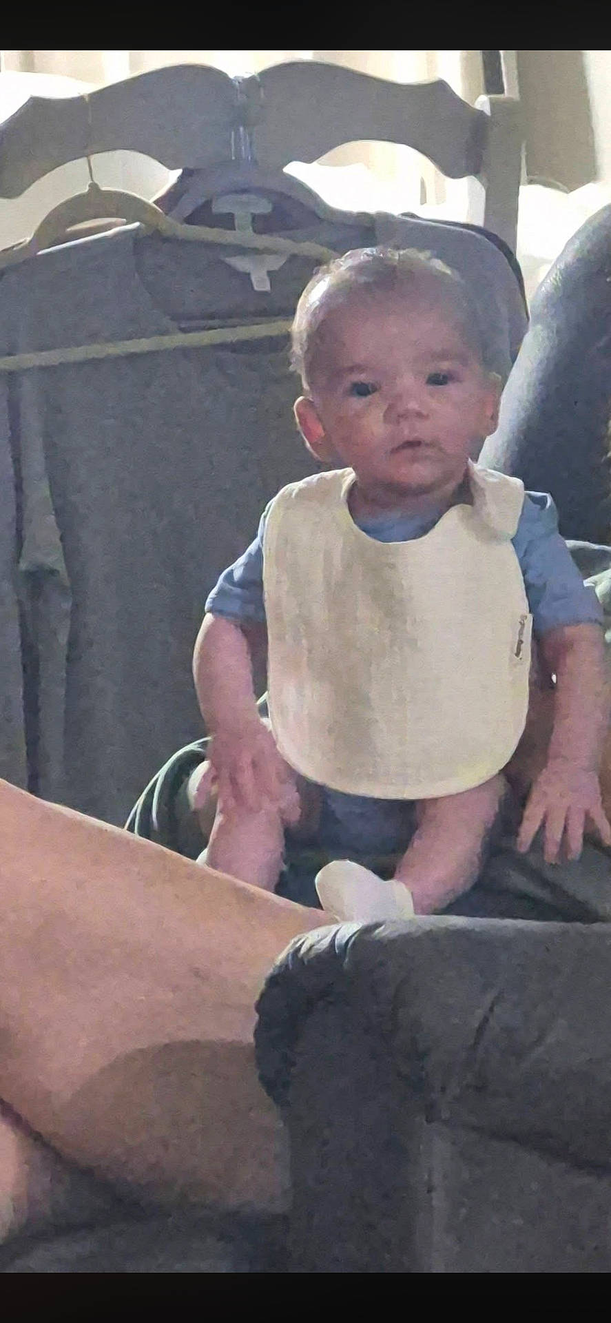 baby, bib, blurry, chair, child, couch, curtain, expression, face, hands, household, indoor, legs, low_light, person, portrait, sitting, sock, sofa, wooden_furniture