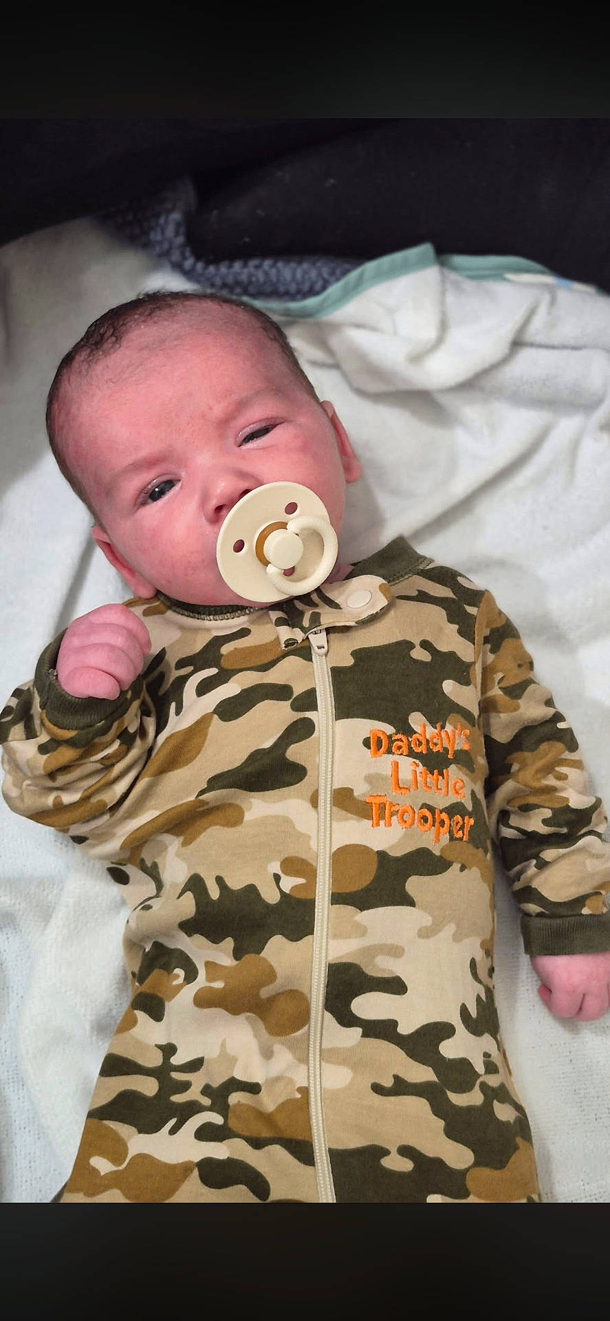 baby, bedding, blanket, camouflage, closeup, cute, embroidery, face, hand, head, indoor, infant_clothing, lying_down, newborn, onesie, pacifier, parenthood, portrait, sleepy, soft_texture