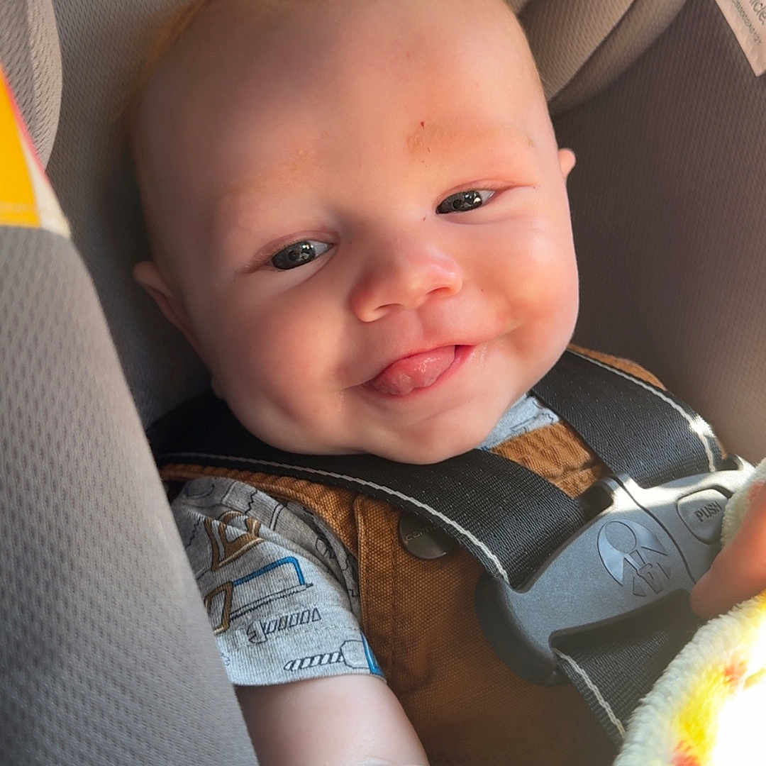 Elizah joined the competition — help win amazing prizes! baby, blanket, car_seat, child, closeup, clothing, cute, face, happy, head, indoors, infant, person, safety, seat, seatbelt, smiling, toddler, tongue_out, young