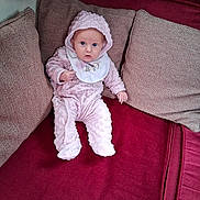 Kimberly joined the competition — help win amazing prizes! baby, infant, pink_clothing, hooded_outfit, bib, couch, cushions, red_fabric, indoor, person, seated, looking_at_camera, cozy, soft_texture, home_interior, child, cute, plush, small_hands, curious