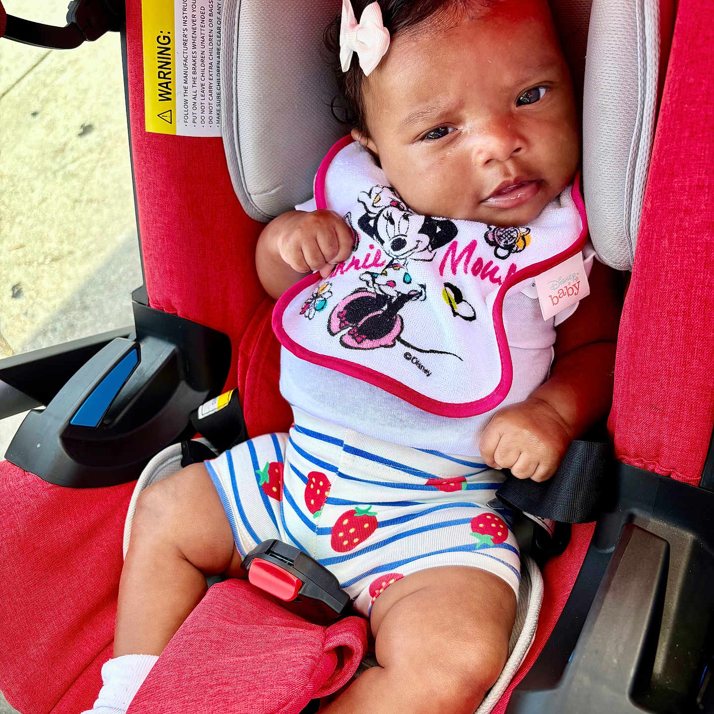 Ramirra is registered to the contest to win money with this photo: baby, infant, child, car_seat, sitting, portrait, smiling, bow, bib, disney, strawberries, striped_clothing, red, pink, white, harness, seat_belt, outdoor, vehicle, safe
