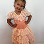 Deynah a rejoint le concours — aidez-le/la à gagner de superbes lots ! child, girl, smile, dress, lace, peach, posing, hands_on_hips, curly_hair, hair_bow, earrings, white_wall, wooden_floor, footwear, happy, portrait, indoor, person, fashion, cute