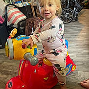Caroline is registered to the contest to win money with this photo: toddler, child, toy_scooter, indoor, playtime, pajamas, minnie_mouse, floor, footwear, smile, face, hand, toy, wheel, furniture, bag, flooring, foot, person, happy