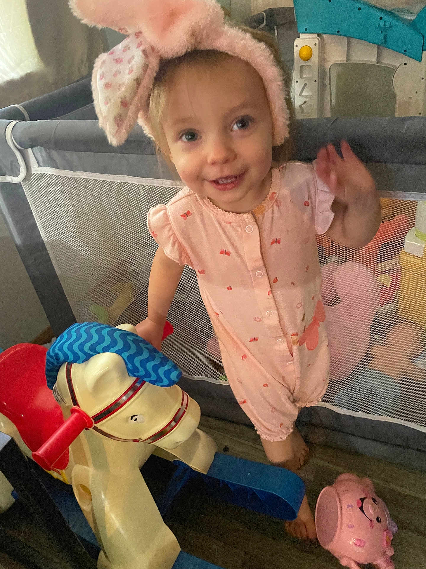 Caroline joined the competition — help win amazing prizes! toddler, child, pink_headband, bunny_ears, onesie, rocking_horse, toy, playpen, smiling, waving, indoor, floor, wood_floor, pink_toy, piggy_bank, happy, cute, young_child, baby, playtime