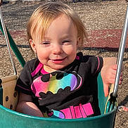 Caroline Cottrill joined the competition — help win amazing prizes! batman_logo, bench, black_tshirt, blonde_hair, casual_clothing, child, daylight, happy, metal_bars, outdoor, park, person, play, playground, rainbow_colors, smiling, sunlight, swing, toddler, wood_chips