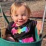 batman_logo, bench, black_tshirt, blonde_hair, casual_clothing, child, daylight, happy, metal_bars, outdoor, park, person, play, playground, rainbow_colors, smiling, sunlight, swing, toddler, wood_chips