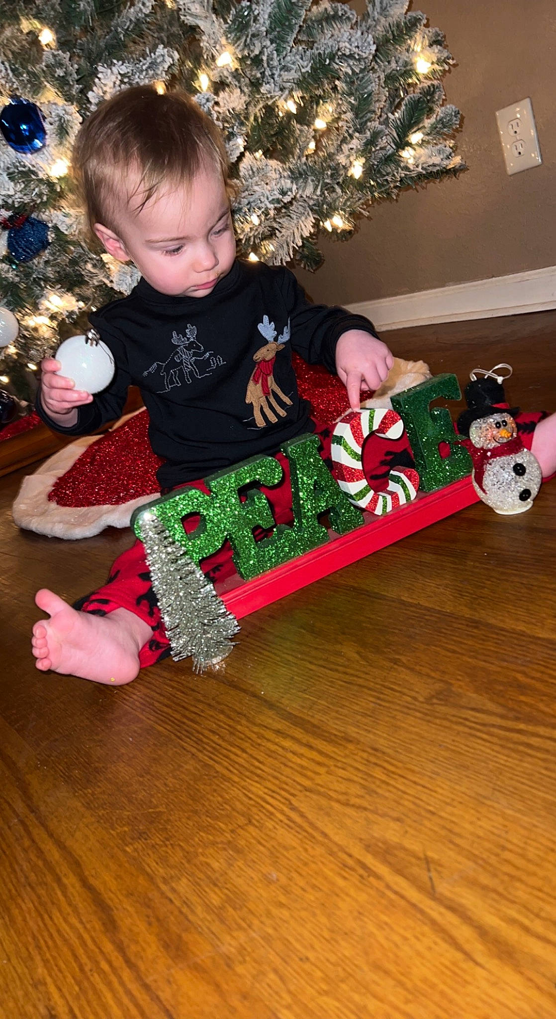Braylynn is registered to the contest to win money with this photo: baby_toddler_clothing, child, christmas, christmas_decoration, christmas_eve, christmas_ornament, christmas_tree, event, fun, hardwood, head, holiday, holiday_ornament, lap, ornament, person, red, sleeve, toddler, white