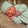 baby, infant, mint_green_clothing, hat, blue_eyes, fluffy_rug, wooden_floor, sleepwear, cute, newborn, soft_texture, portrait, lying_down, face, hand, skin, expression, cozy, indoors, closeup