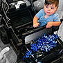 toddler, child, toy_car, blue_ribbons, balloons, indoor, floor, wooden_floor, black_car, curious, rosy_cheeks, short_hair, blue_shirt, calvin_klein, hands, eyes, face, birthday, celebration, gift