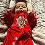 baby, infant, red_onesie, reindeer_design, floral_pattern, cushion, blanket, soft_texture, cozy, lying_down, hands, face, cute, holiday_theme, indoors, portrait, child, warm, comfortable, sleepwear