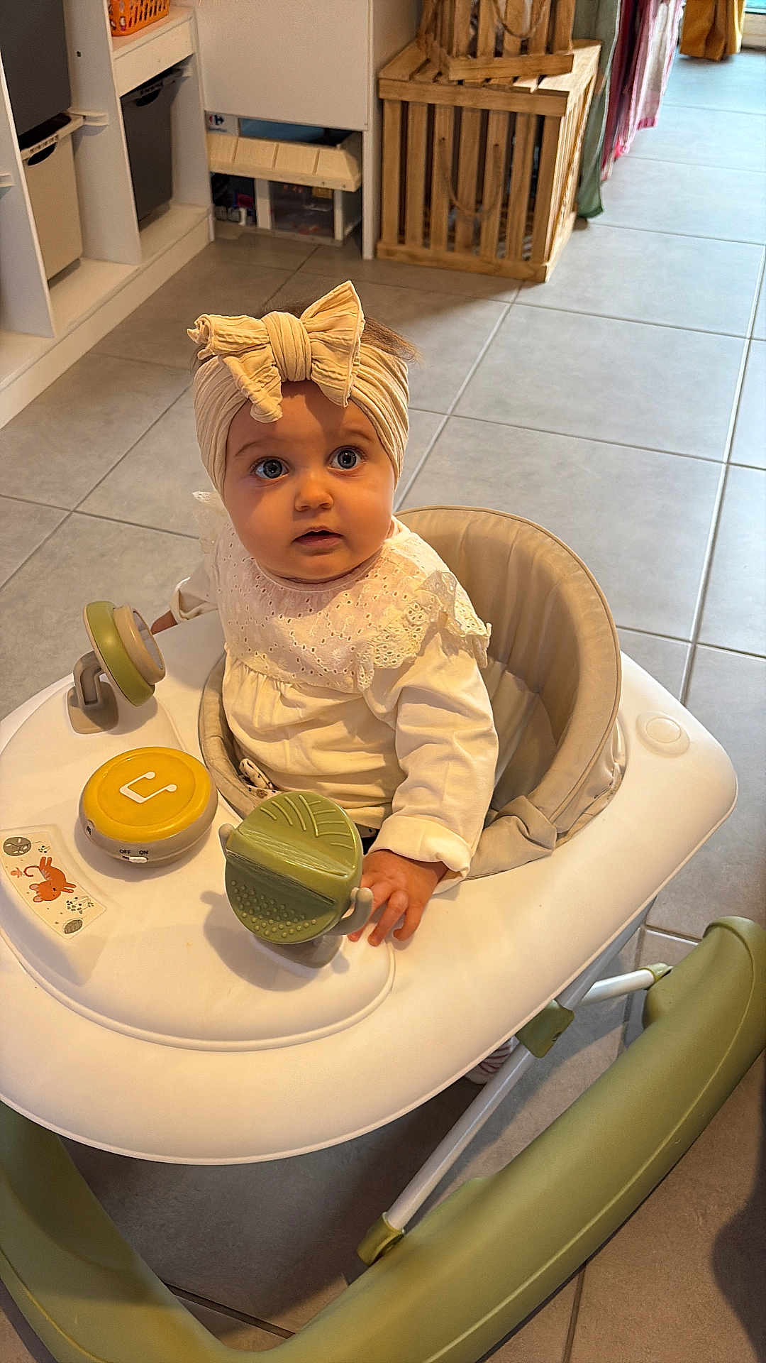 Tysaée participe au concours pour gagner de l'argent avec cette photo : baby, bow, child, clothing, curious, cute, floor, green, hand, headband, indoor, infant, looking_up, person, portrait, seat, tile, toy, walker, white