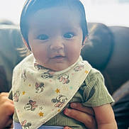 Hulani is registered to the contest to win money with this photo: baby, child, infant, person, face, bib, clothing, green_shirt, hand, sitting, indoor, soft_lighting, cute, smile, mickey_mouse, pattern, couch, background_blur, portrait, young