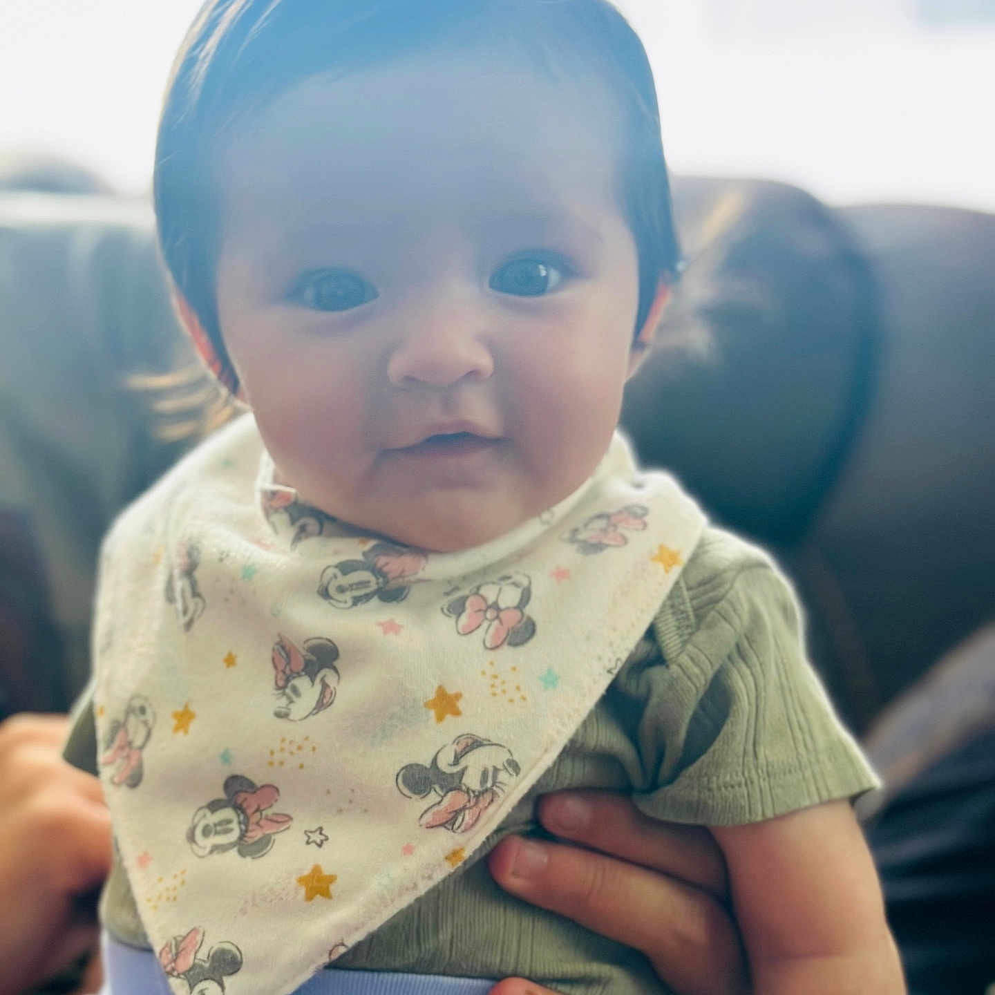 Hulani is registered to the contest to win money with this photo: baby, background_blur, bib, child, clothing, couch, cute, face, green_shirt, hand, indoor, infant, mickey_mouse, pattern, person, portrait, sitting, smile, soft_lighting, young