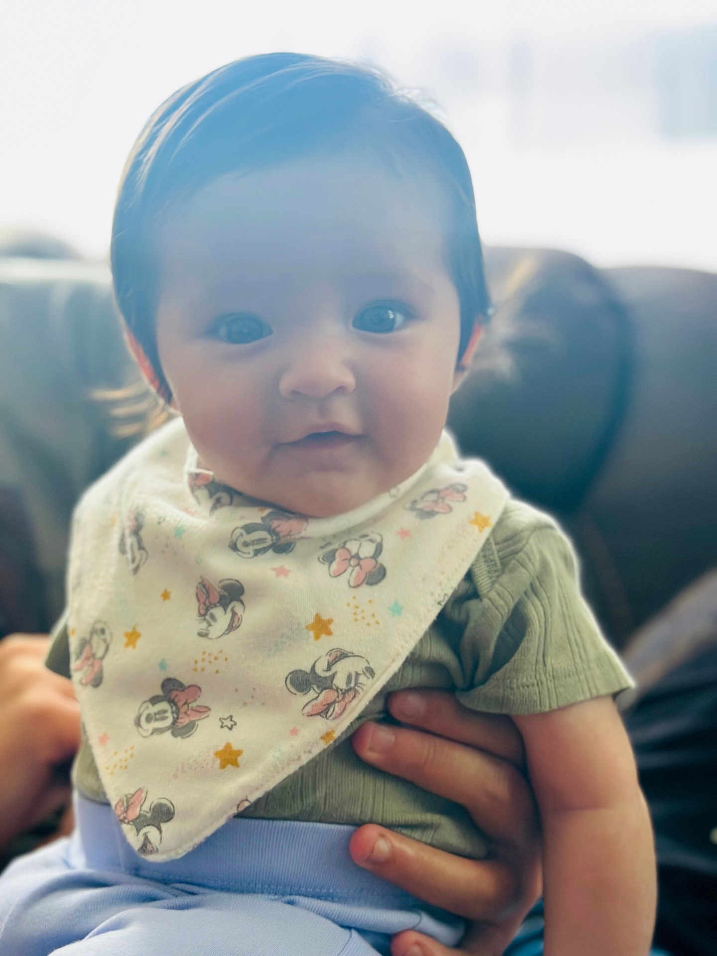 Hulani is registered to the contest to win money with this photo: baby, child, infant, person, face, bib, clothing, green_shirt, hand, sitting, indoor, soft_lighting, cute, smile, mickey_mouse, pattern, couch, background_blur, portrait, young