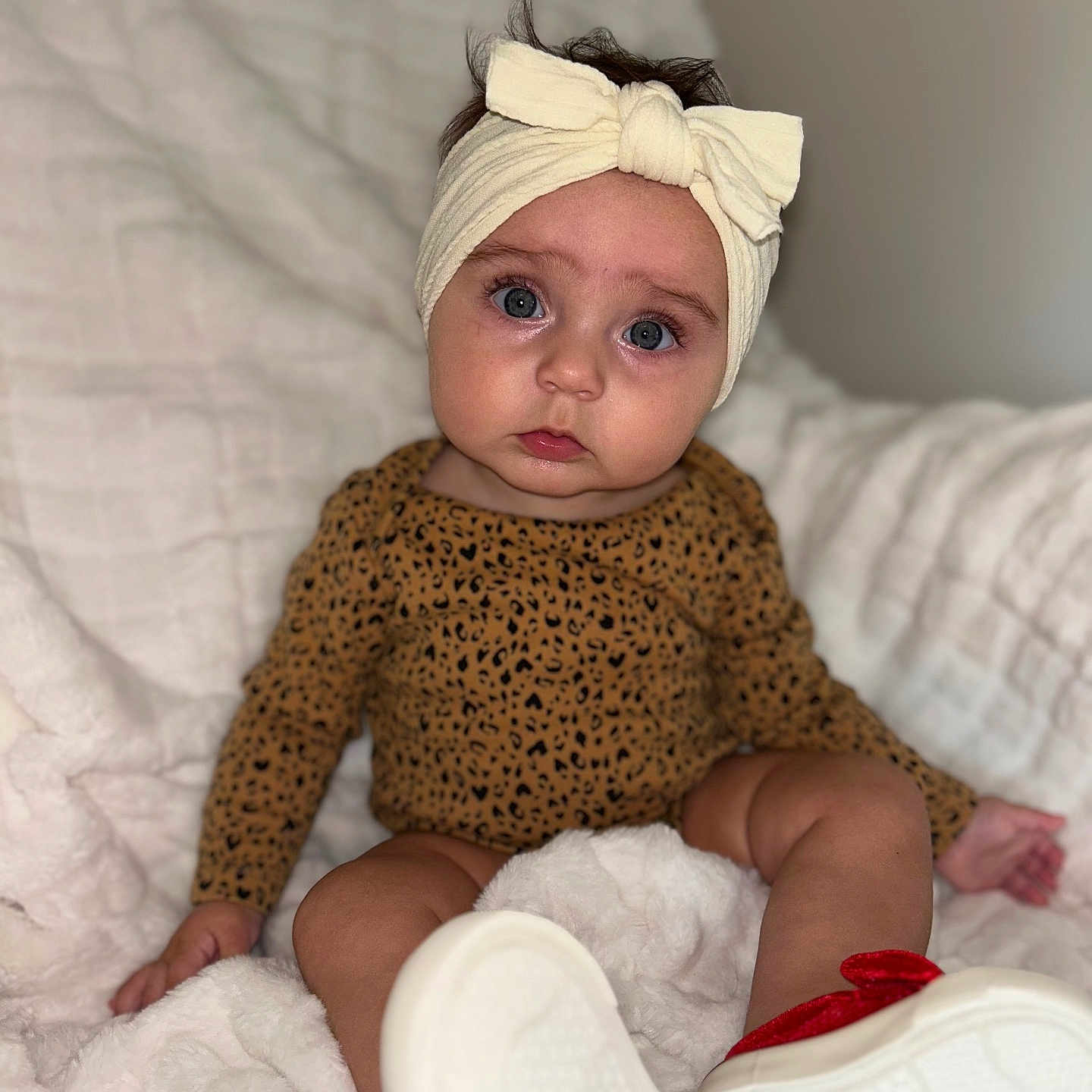 Gracie is registered to the contest to win money with this photo: baby, blanket, bow, child, clothing, cozy, cute, expression, face, footwear, headband, indoors, infant, leopard_print, person, portrait, red_shoes, sitting, soft_texture, white