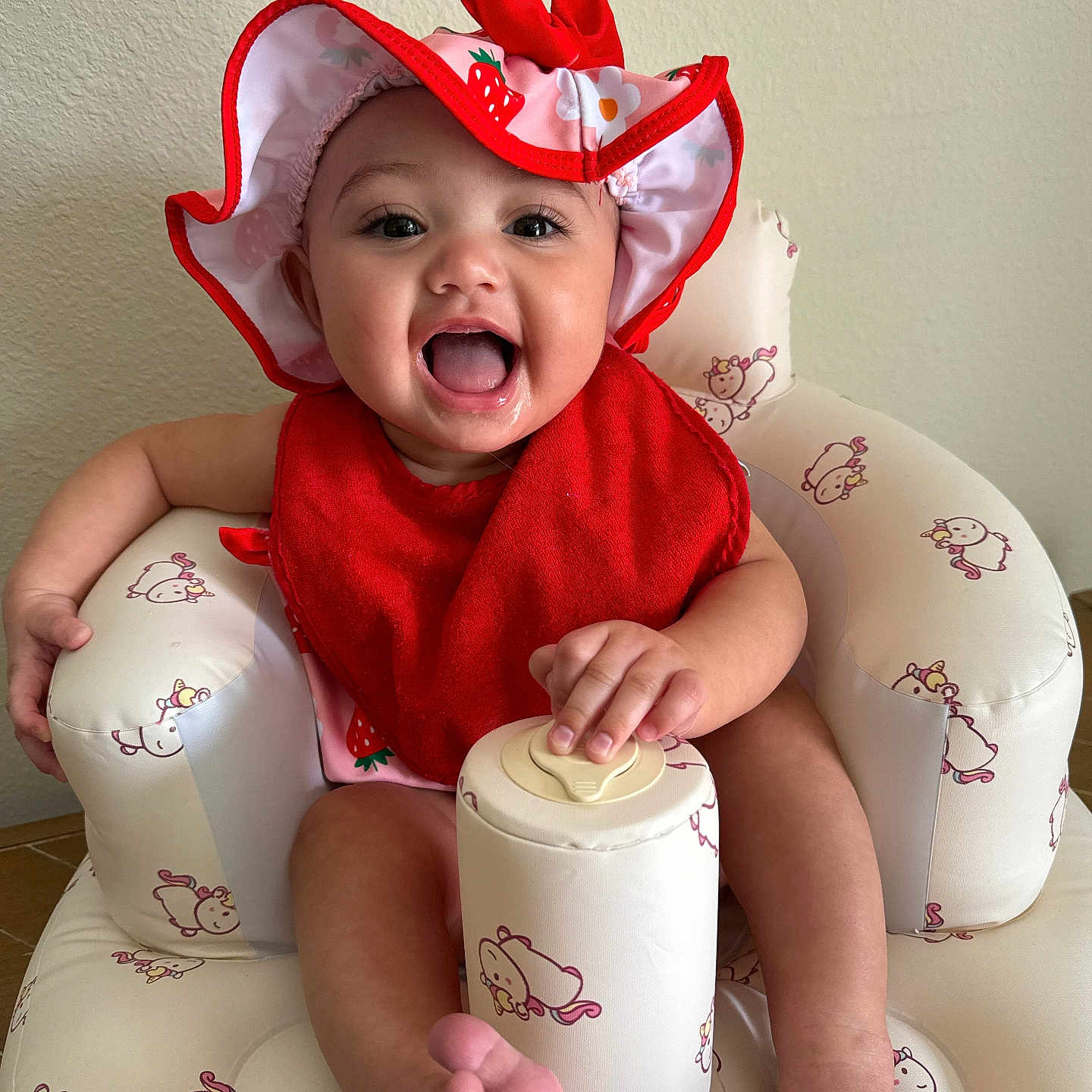 Airalee is registered to the contest to win money with this photo: baby, child, cute, face, foot, hand, happy, hat, indoor, infant, inflatable_chair, person, pink, playful, red, red_bib, sitting, smiling, unicorn_pattern, young