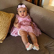 Siara joined the competition — help win amazing prizes! baby, child, infant, pink_dress, headband, couch, pillow, socks, flower, indoor, furniture, person, cute, portrait, happy, young, seated, home, expression, legs