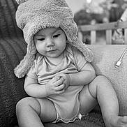 Malilou a rejoint le concours — aidez-le/la à gagner de superbes lots ! baby, child, infant, hat, fuzzy_hat, pom_poms, sitting, blanket, indoors, couch, monochrome, black_and_white, cute, portrait, clothing, hands, legs, expression, soft_texture, cozy