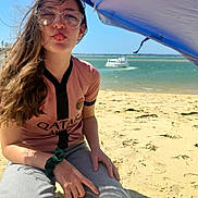 Ilona participe au concours pour gagner de l'argent avec cette photo : child, beach, sand, umbrella, glasses, tongue_out, hair, boat, water, sky, crouching, casual_clothing, scrunchie, sunny, outdoor, playful, youth, portrait, sports_jersey, fun