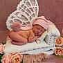 baby, newborn, sleeping, pink_hat, pom_pom, miniature_chaise_lounge, white_furniture, roses, flowers, lace, butterfly_wings, soft_texture, fluffy, cute, infant, decor, portrait, peaceful, resting, indoors