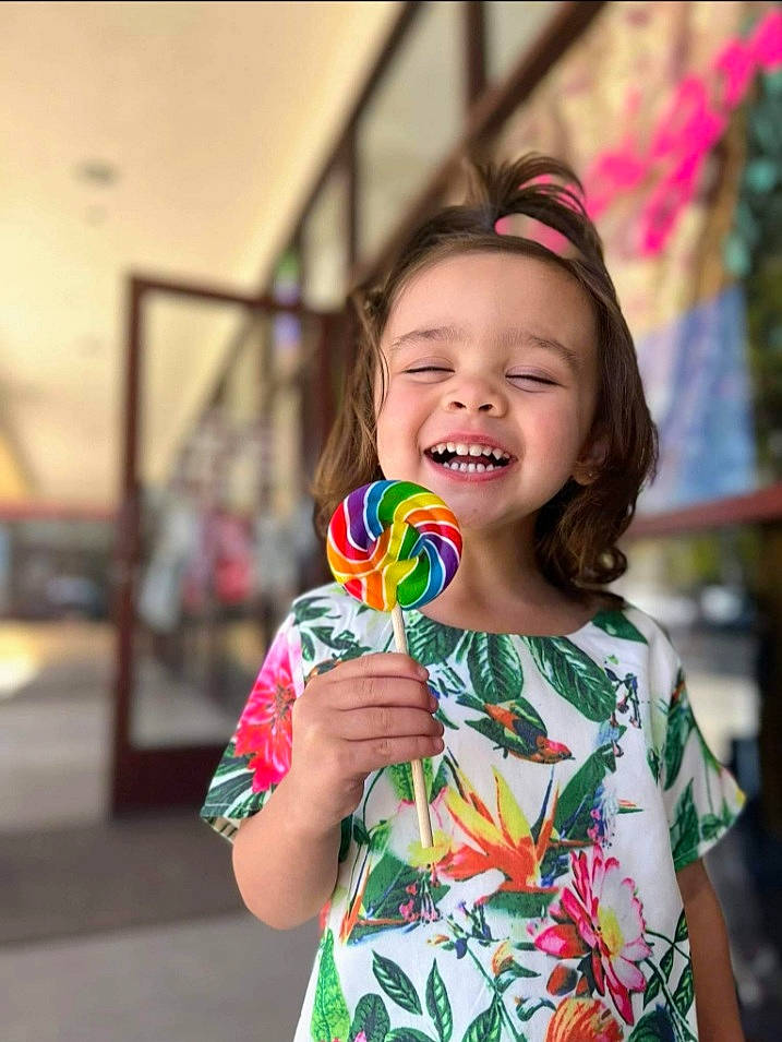 Harley is registered to the contest to win money with this photo: child, dress, event, facial_expression, finger, fun, grass, hand, happy, holiday, iris, joy, lollipop, pattern, people, person, photograph, pink, smile, summer