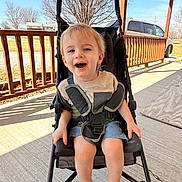 Rylee joined the competition — help win amazing prizes! casual_clothing, child, concrete, daytime, happy, nature, outdoor, person, porch, railing, seatbelt, shorts, sky, smiling, stroller, sunlight, toddler, trees, vehicle, young_child