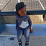child, boy, cap, sweatshirt, tiger_design, bench, outdoor, sidewalk, shoes, pants, metal_bench, fence, parking_lot, casual_clothing, daylight, urban, young_child, looking_away, seated, curious