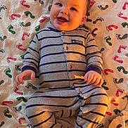 Jackson Jr. is registered to the contest to win money with this photo: baby, smiling, pajamas, striped_clothing, blanket, footprint_pattern, lying_down, happy, infant, child, cute, indoors, warm_light, portrait, one_person, baby_clothes, soft_texture, cheerful, human, small_hands