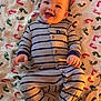 baby, smiling, pajamas, striped_clothing, blanket, footprint_pattern, lying_down, happy, infant, child, cute, indoors, warm_light, portrait, one_person, baby_clothes, soft_texture, cheerful, human, small_hands