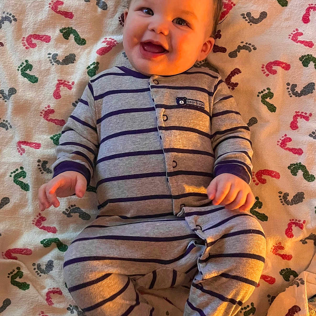 Jackson Jr. is registered to the contest to win money with this photo: baby, baby_clothes, blanket, cheerful, child, cute, footprint_pattern, happy, human, indoors, infant, lying_down, one_person, pajamas, portrait, small_hands, smiling, soft_texture, striped_clothing, warm_light