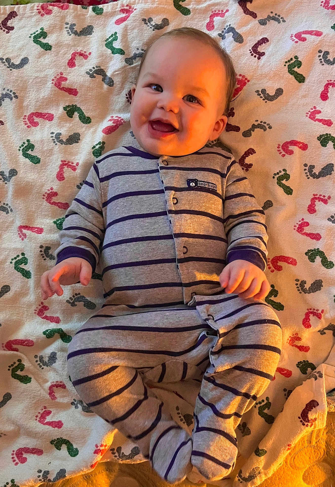 Jackson Jr. is registered to the contest to win money with this photo: baby, smiling, pajamas, striped_clothing, blanket, footprint_pattern, lying_down, happy, infant, child, cute, indoors, warm_light, portrait, one_person, baby_clothes, soft_texture, cheerful, human, small_hands
