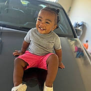 Liam joined the competition — help win amazing prizes! toddler, child, smiling, happy, sitting, car, hood, gray_shirt, pink_shorts, white_shoes, indoor, garage, reflection, cute, person, portrait, hair_buns, footwear, casual_clothing, young_child