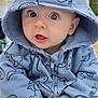 baby, child, hoodie, blue_clothing, dinosaur_pattern, hand_holding, outdoor, curious_expression, face, person, infant, cute, portrait, sitting, hood, big_eyes, young_child, casual_clothing, human, closeup