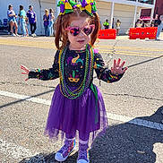 Aurora joined the competition — help win amazing prizes! child, girl, toddler, heart_sunglasses, mardi_gras_beads, purple_tutu, bows, pigtails, colorful_outfit, patterned_top, purple_sneakers, street, parade, crowd, daylight, decorations, building, sunny, shadow, mask_design