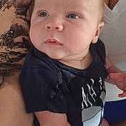 Curtis is registered to the contest to win money with this photo: baby, infant, person, arm, tattoo, shirt, clothing, holding, skin, face, portrait, child, human, closeup, casual, indoor, cute, newborn, expression, family